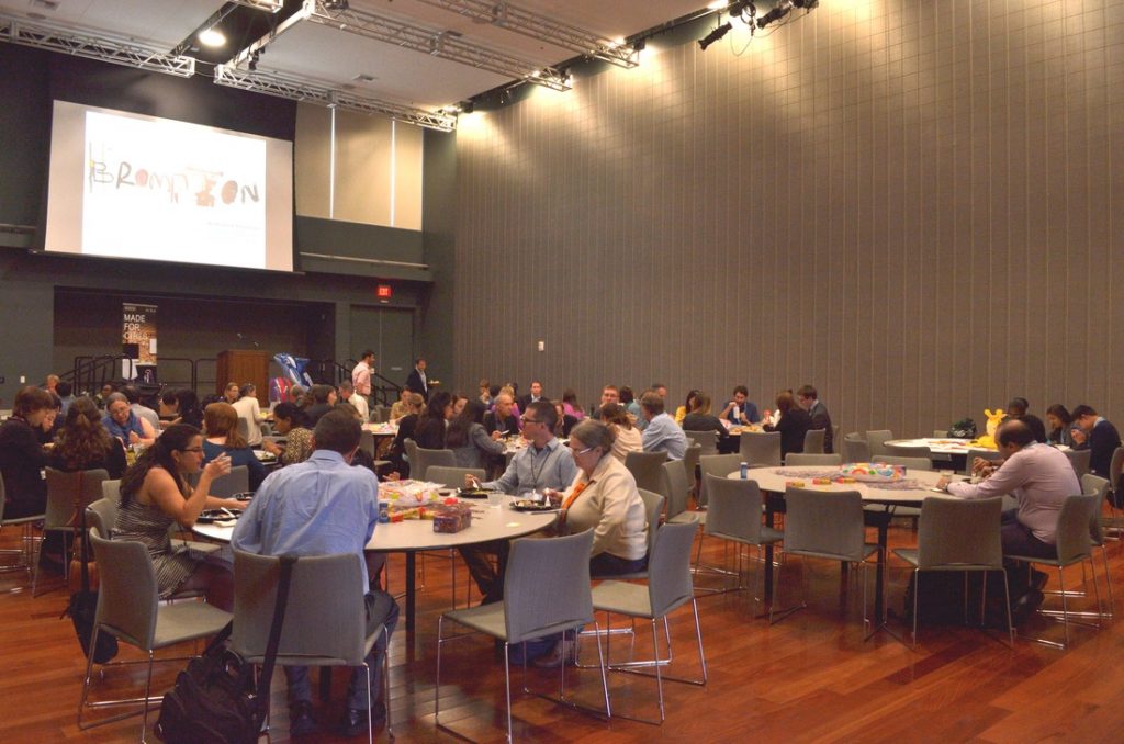 People sitting at round tables in a hall, taking part in a workshop