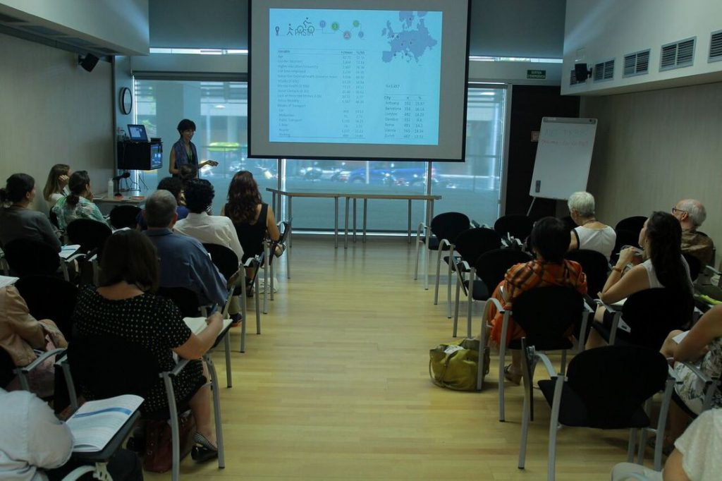 Rows of people all facing a projector screen whilst a lady gives a presentation