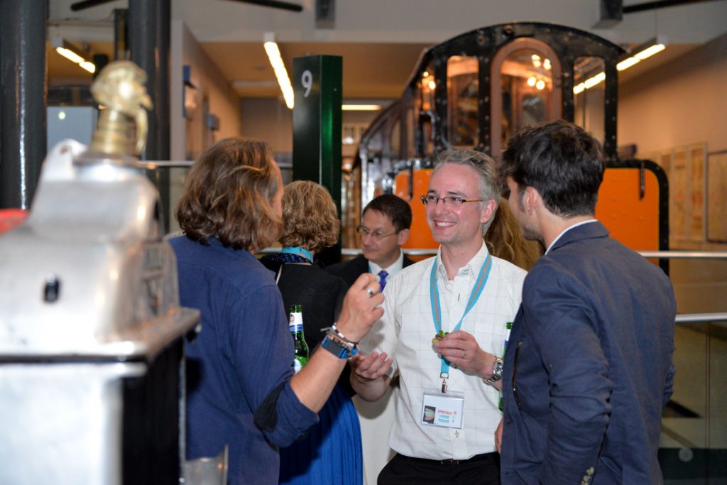 4 men and one woman enjoying evening drinks and informally chatting in a transport museum