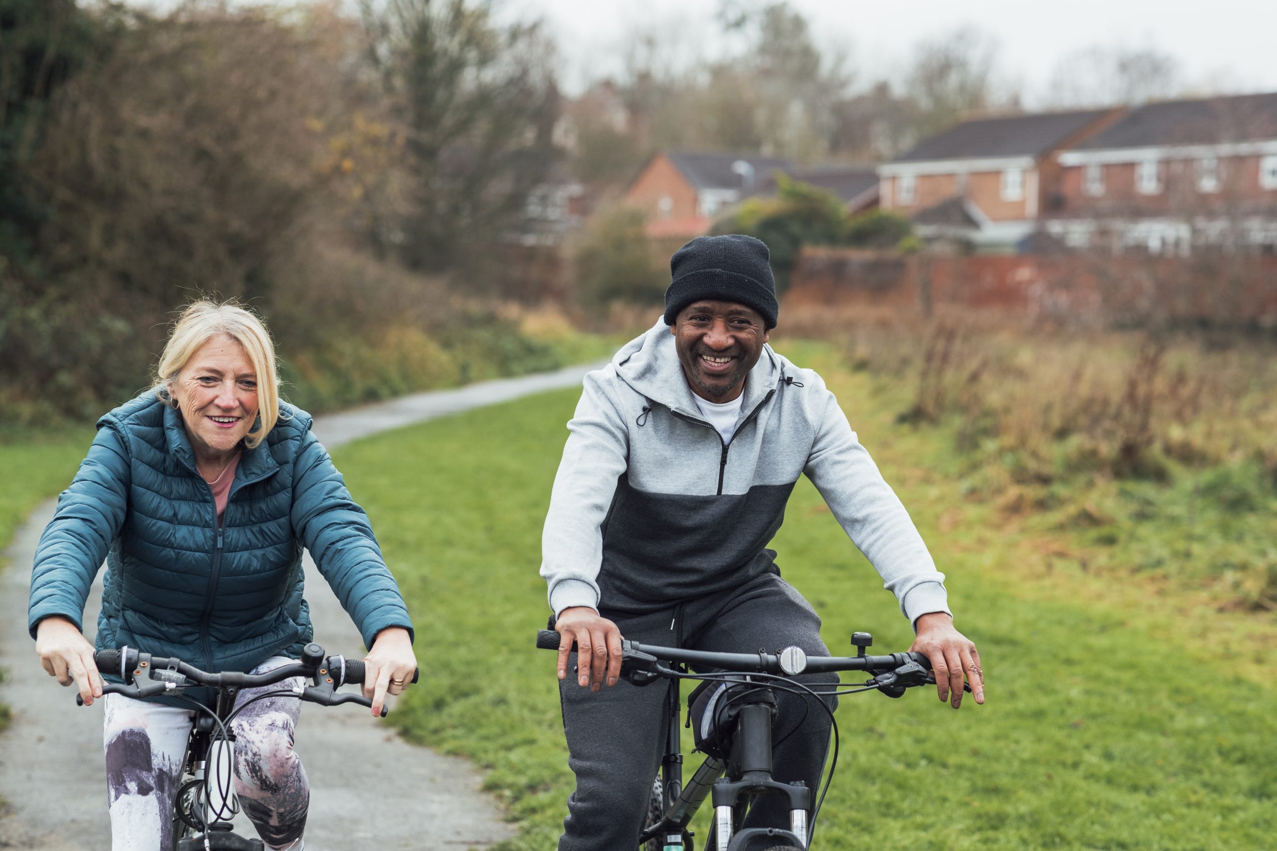 A senior multi-ethnic couple wearing casual sporty clothing and cycling through their local park on a morning in December.