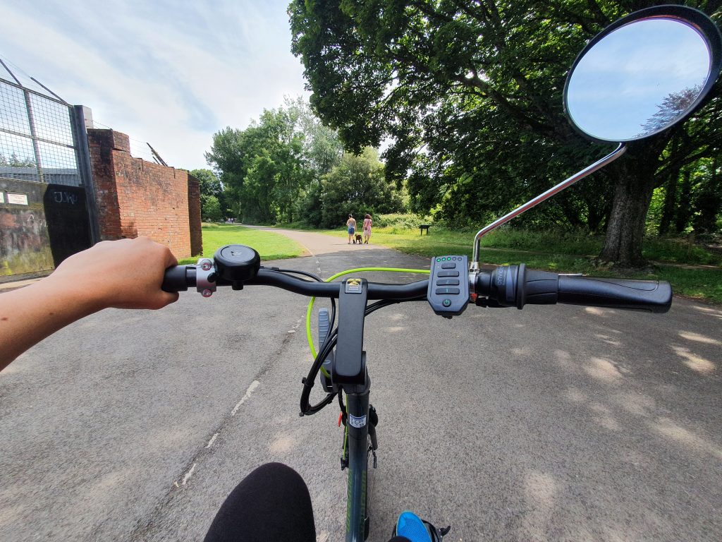 Photo of handlebars of electric bicycle whilst being cycled through a park